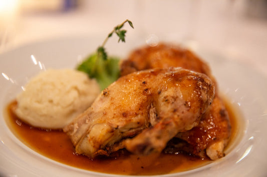 Roasted chicken with mashed potatoes and gravy on a white plate.