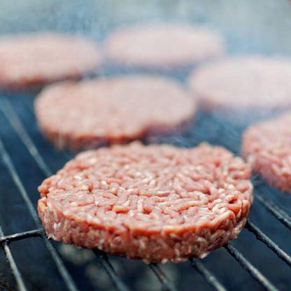 100% grass-fed beef patties cooking on a grill with smoke rising around the burgers.