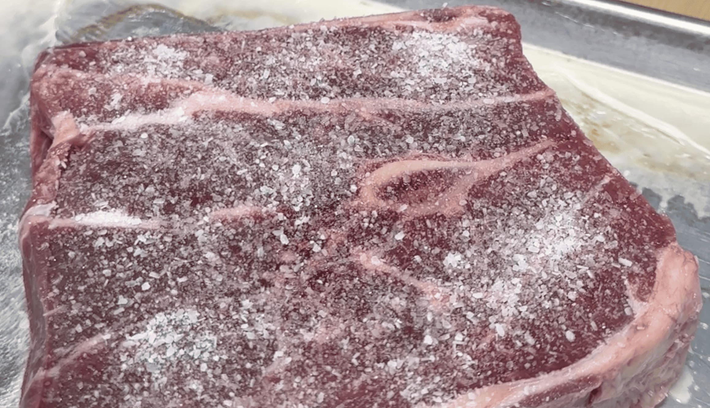 Raw beef steak seasoned with salt on a metal surface