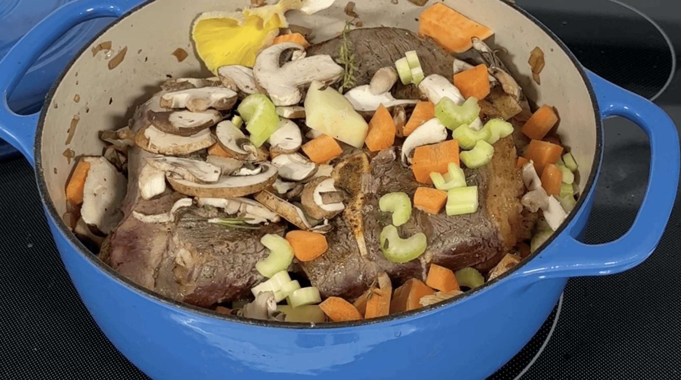 Blue pot with beef, mushrooms, carrots, and celery on a stove