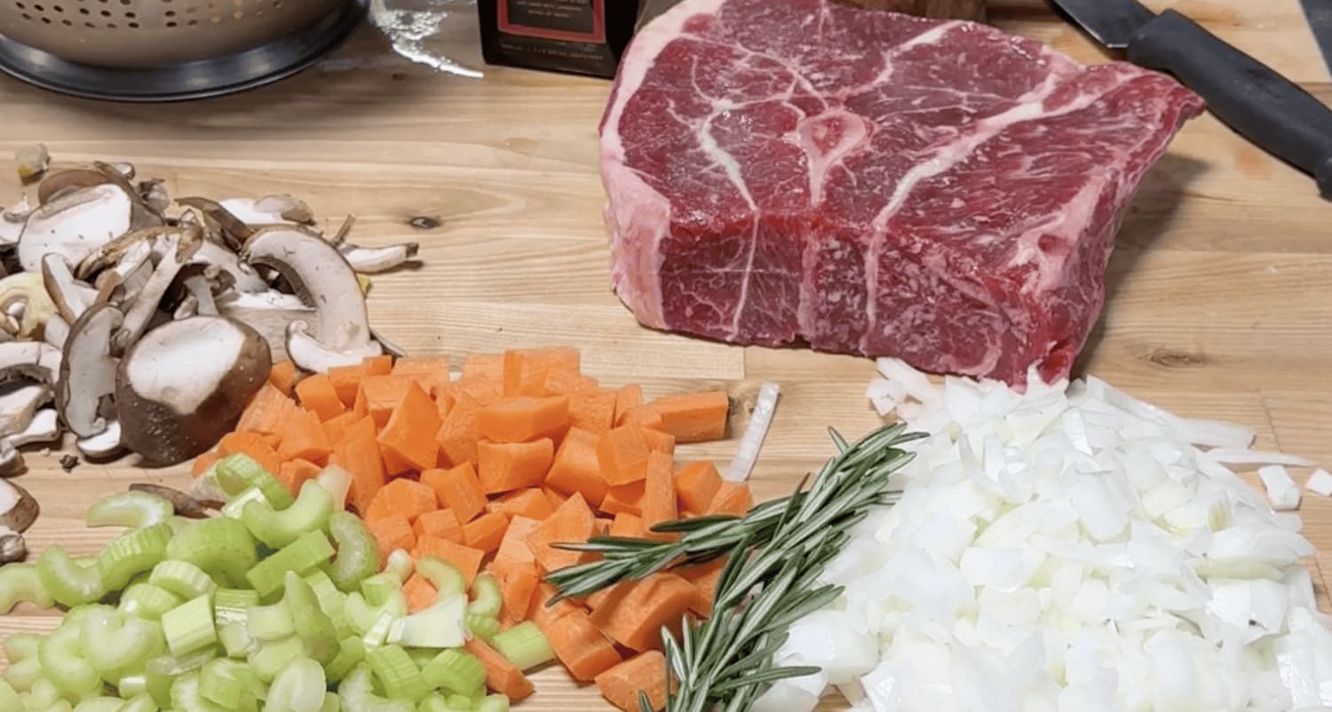 Raw steak with chopped vegetables on a wooden cutting board