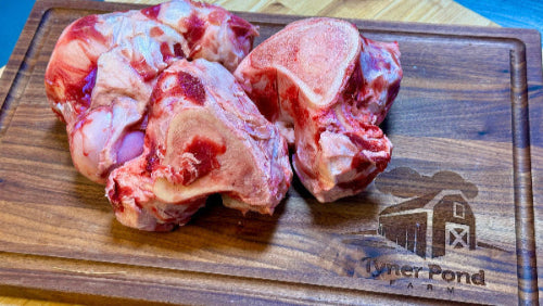 Raw meat bones on a wooden cutting board with 'Tyner Pond Farm' branding.