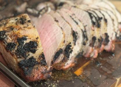 Sliced roasted pork on a wooden cutting board with a knife in the background.