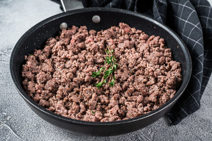 Grassfed Ground beef in a black frying pan on a gray surface with a checkered towel.
