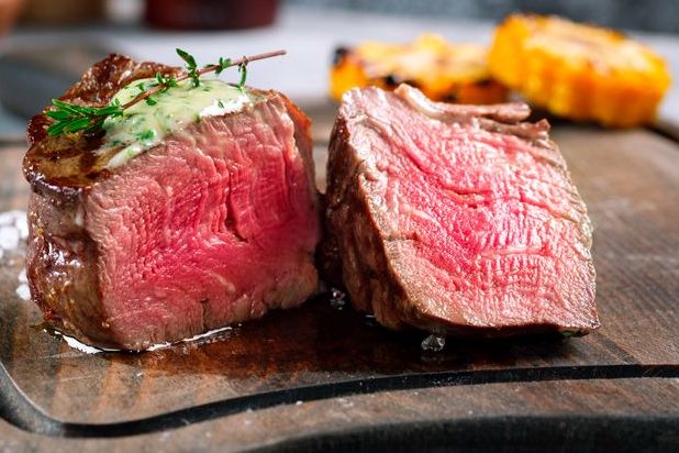 Sliced grassfed filet steak with a creamy herb topping on a wooden cutting board