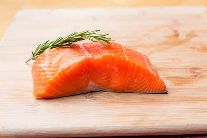 Raw wild caught salmon fillet on a wooden cutting board with rosemary