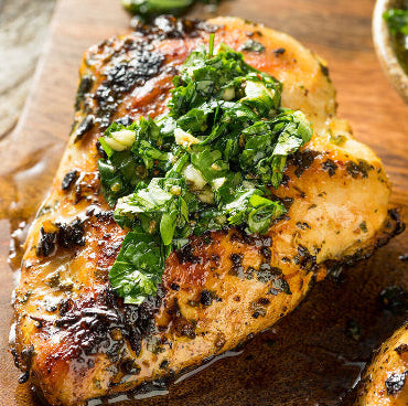 Perfectly cooked pasture-raised chicken breast on plate, lightly seasoned with green herb sauce