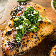 Perfectly cooked pasture-raised chicken breast on plate, lightly seasoned with green herb sauce