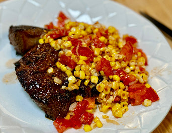 Cooked sirloin steak plated with corn and red pepper medley, grassfed beef