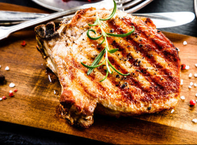 Cooked pork chop resting on wooden cutting board, juicy and ready to slice