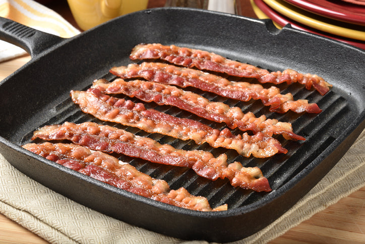 Bacon frying in pan, sizzling and curling with natural fat