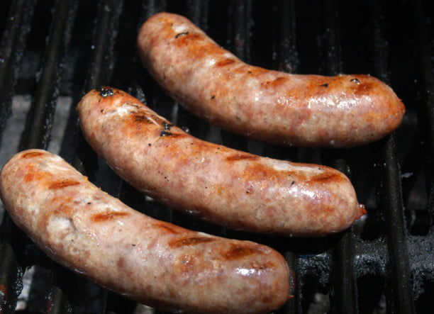 Top-down view of bratwurst grilling on barbecue, browning evenly