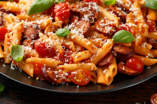 Pasta dish with red sauce and sliced hot Italian sausage, plated and garnished
