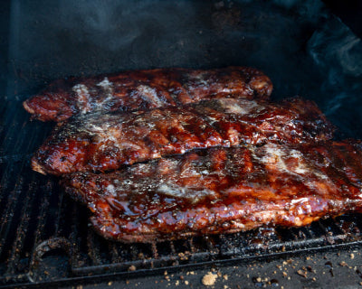 Pork spare ribs smoking on grill with visible bark forming, uncooked and unseasoned