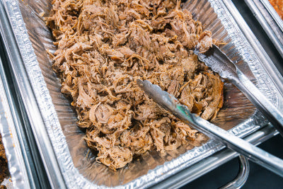 Top-down view of pulled pork in foil container, fully cooked and ready to serve