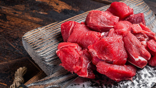 Raw stew meat chunks on wooden cutting board, cut from grassfed beef