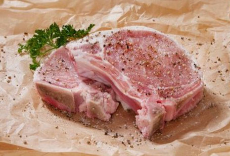 Two raw bone-in pork chops seasoned with salt and pepper on butcher paper