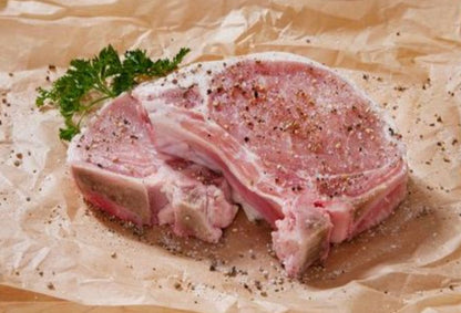 Two raw bone-in pork chops seasoned with salt and pepper on butcher paper