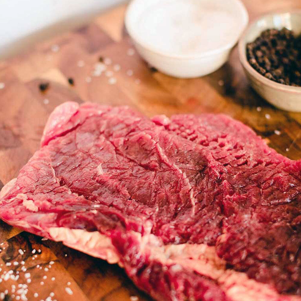 Raw top round steak on wooden cutting board, lean and grassfed