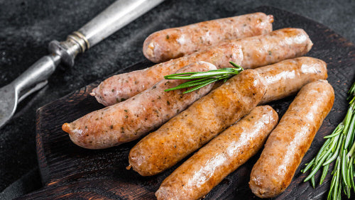Raw Jamaican bratwurst links on cutting board, showing tropical sausage blend