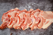 Six raw bone-in pork chops laid out on counter, fresh and trimmed