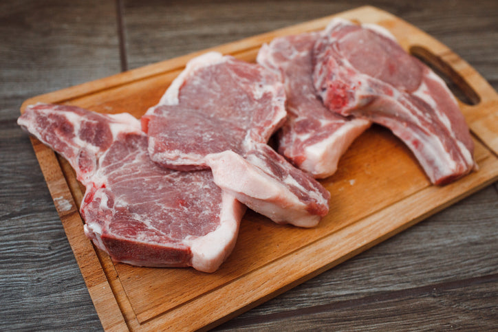 Raw pork chops on cutting board, included in Tyner Pond Farm small pork bundle