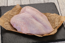 Raw skin-on turkey breast on parchment paper on a black slate board.